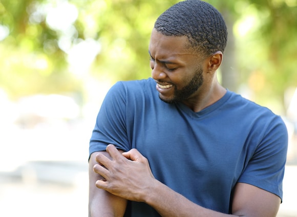 Black man scratching itchy arm in a park