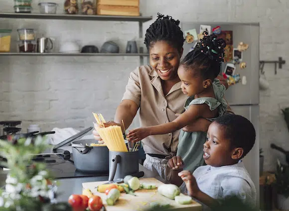 Happy African American mother, daughter and son preparing spaghetti and vegetables for lunch