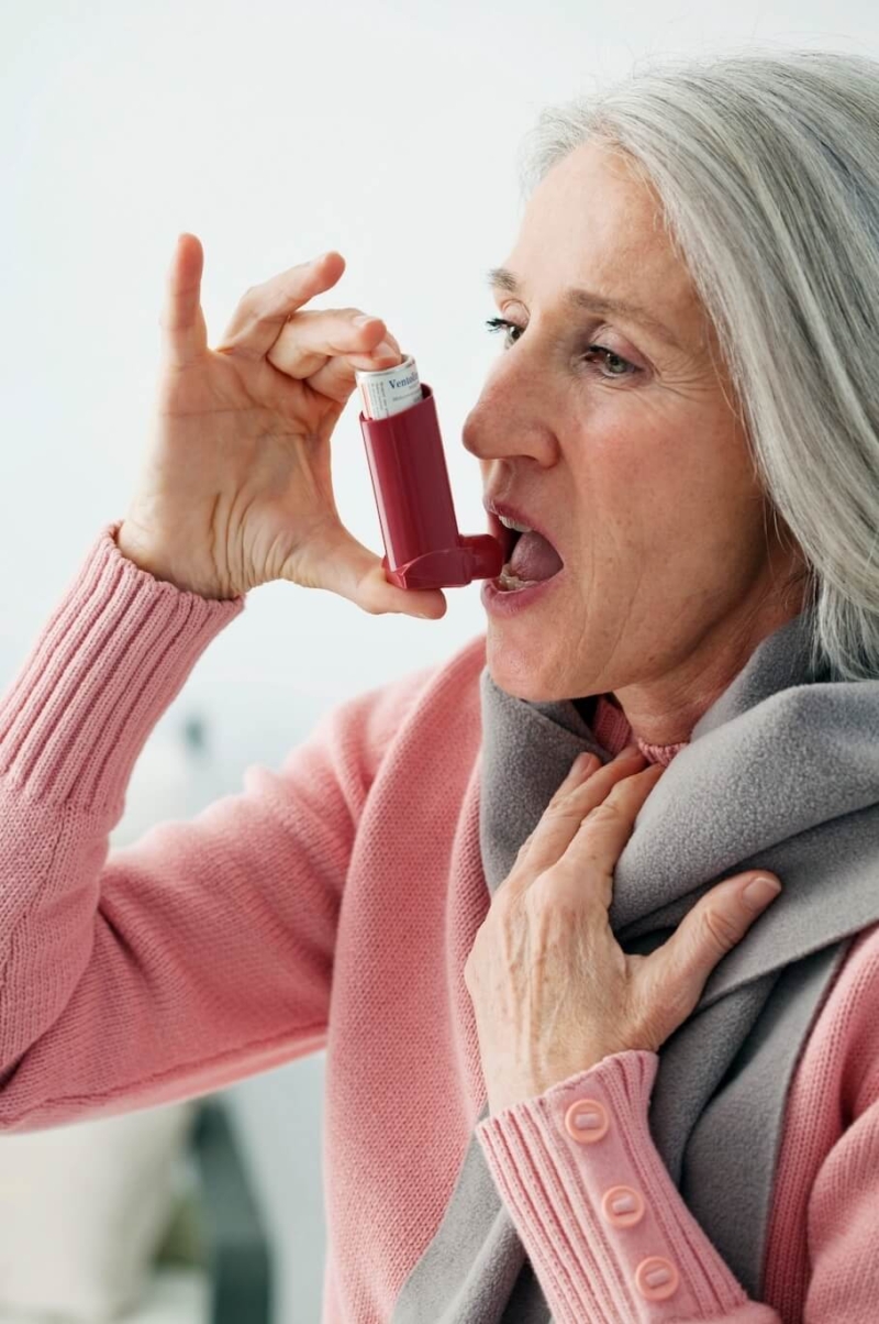 Senior woman in pink sweater using an asthma inhaler
