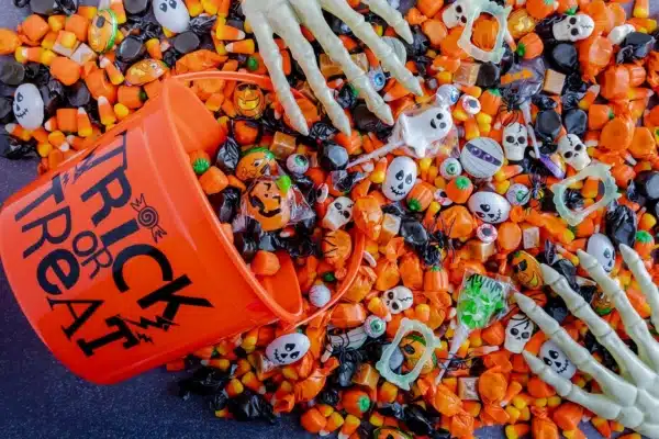 Orange trick or treat pail spilling Halloween candy on black stone surface