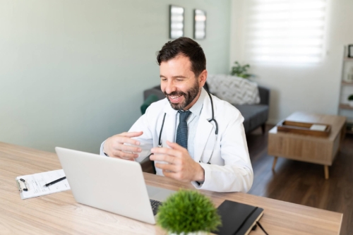 Friendly Hispanic doctor working from home and talking to a patient in a telemedicine consultation