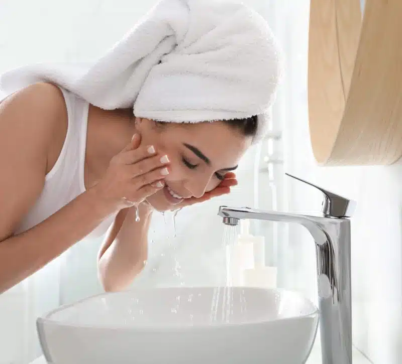 Happy young woman washing face in bathroom