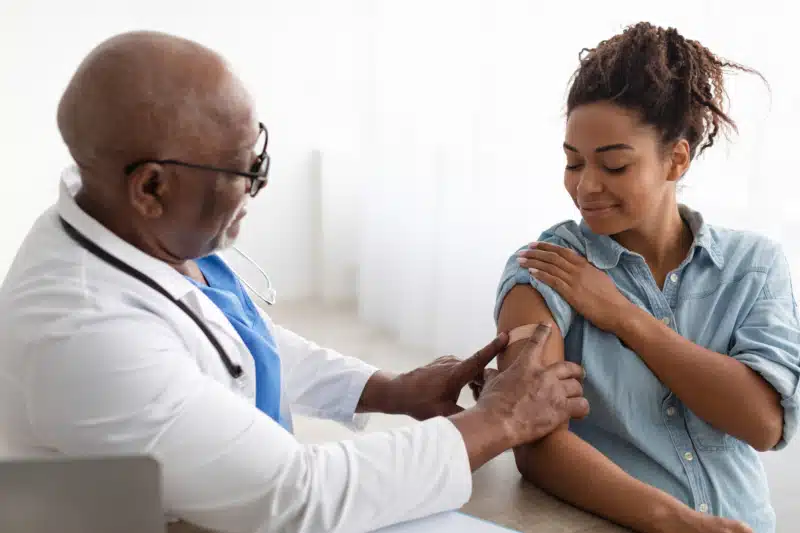 Doctor placing a band aid on a black lady's arm after getting immunotherapy allergy shots