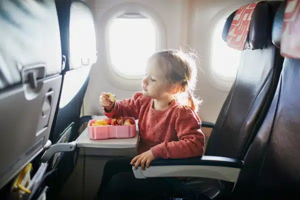 Preschooler girl eating snacks from lunch box while traveling by plane