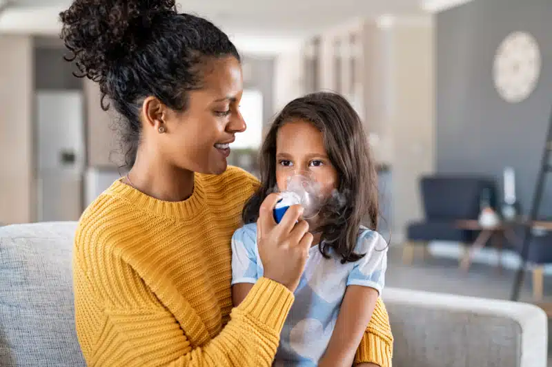 Mother and daughter sitting on a couch, mother is helping daughter with her nebulizer