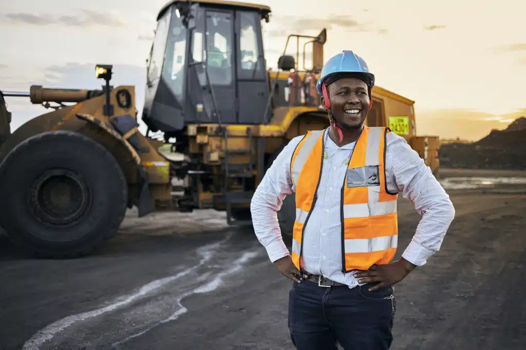 Construction worker smiling with a construction vehicle in the back