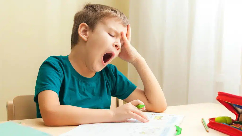Little boy of around 5 years of age yawning while trying to do homework on a dining room table