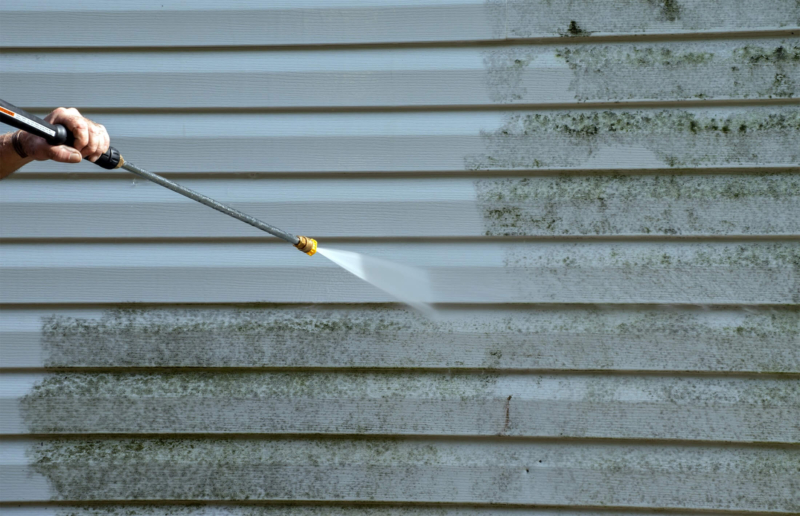 Handyman cleaning outdoor mold from vinyl siding on an exterior wall of a house with a pressure washer