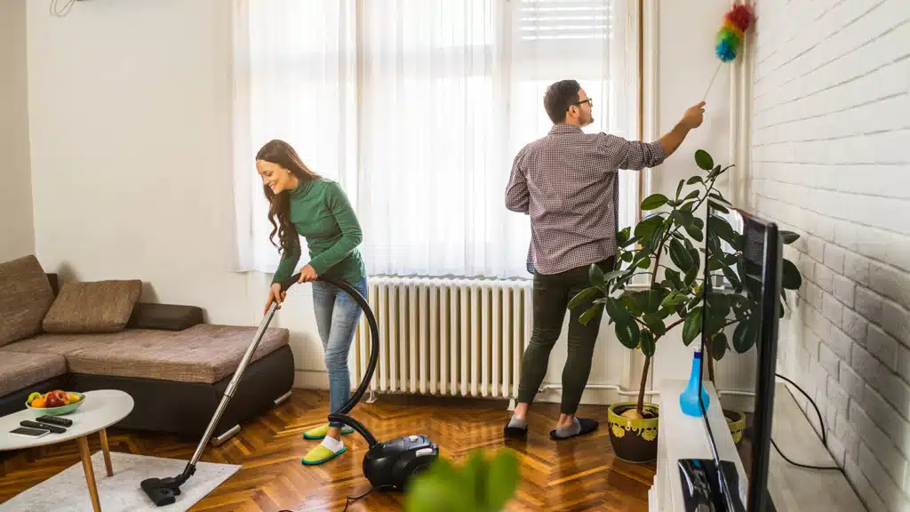 Couple cleaning the living room of an apartment with a vacuum cleaner and a cleaning duster