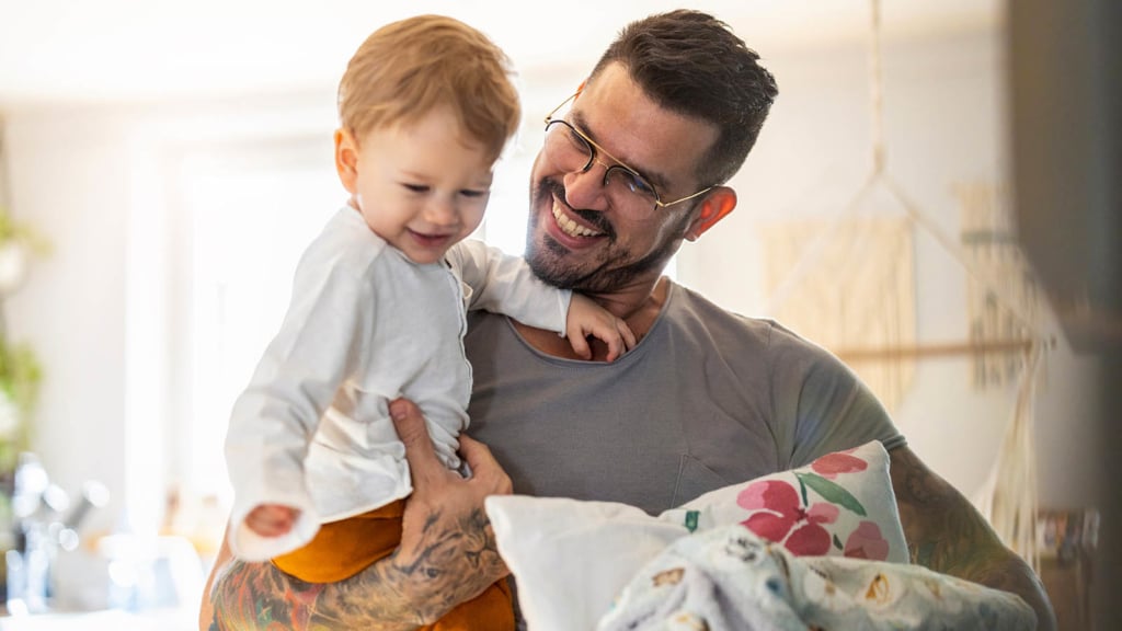 Happy father holding a happy toddler and a pillow and blanket