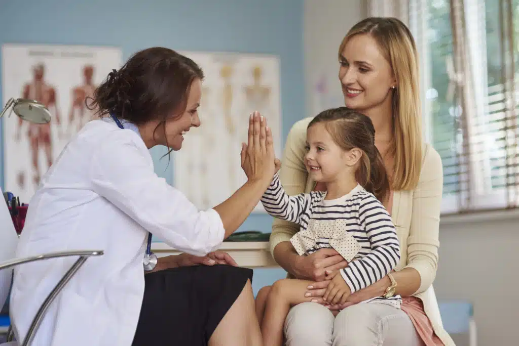 Female doctor high-fiving a child asthma patient sitting on her mother's lap
