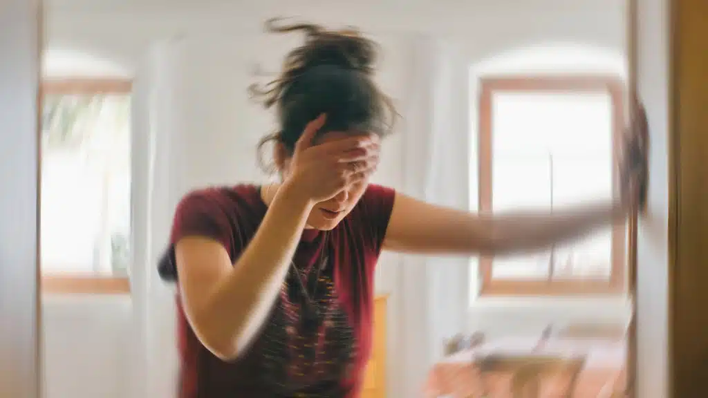 Woman looking dizzy grabbing her forehead with one hand and leaning to the wall with the other hand due to a drug allergy reaction
