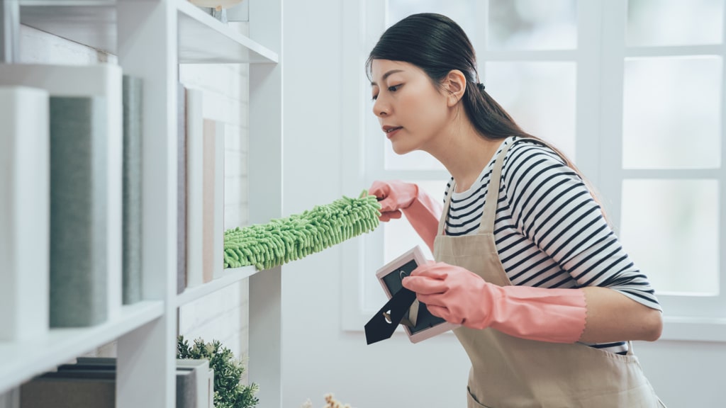 Woman cleaning dust off book shelf with a green cleaning duster