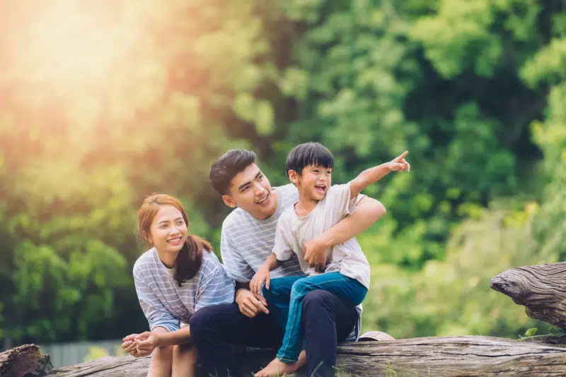 Happy harmonious family, mother, father and little boy sitting on a tree log in the woods