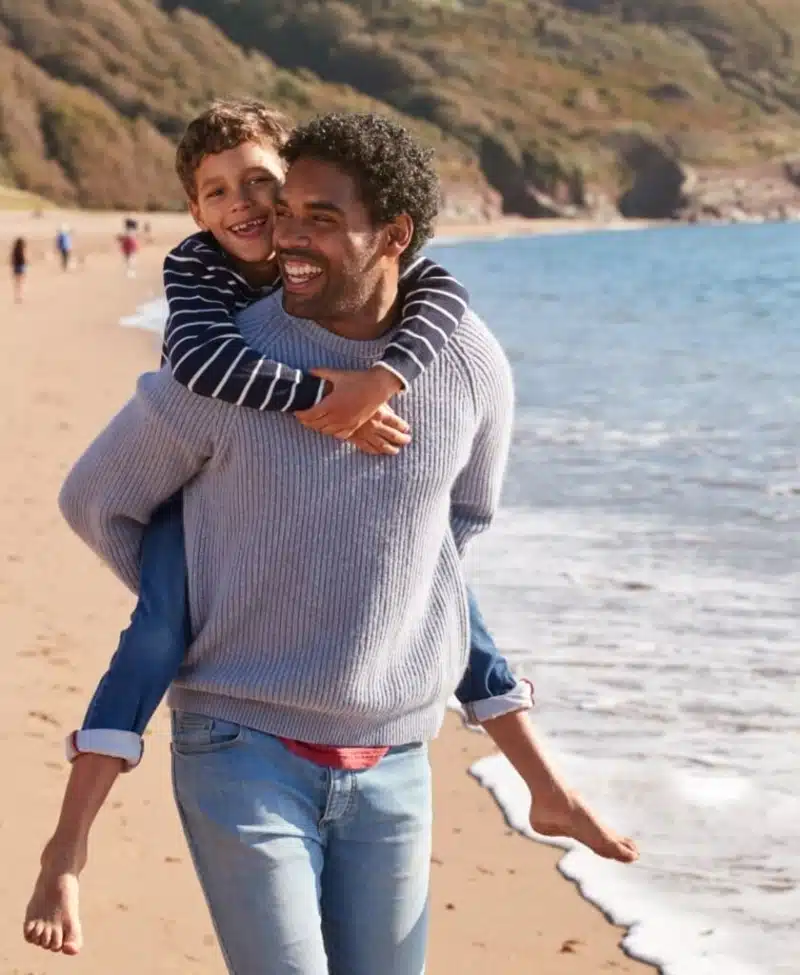 Loving father giving son piggyback as they walk along at the beach