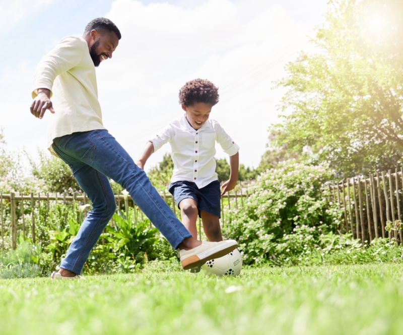 father and son playing soccer together outdoors