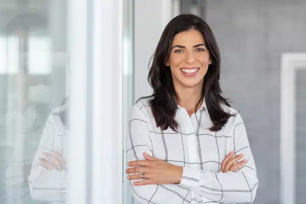 Confident business woman with arms crossed standing while leaning against glass wall.