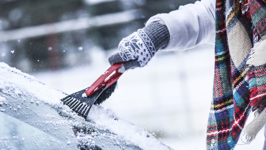 Person cleaning snow caused by extreme weather conditions off a car's windshield