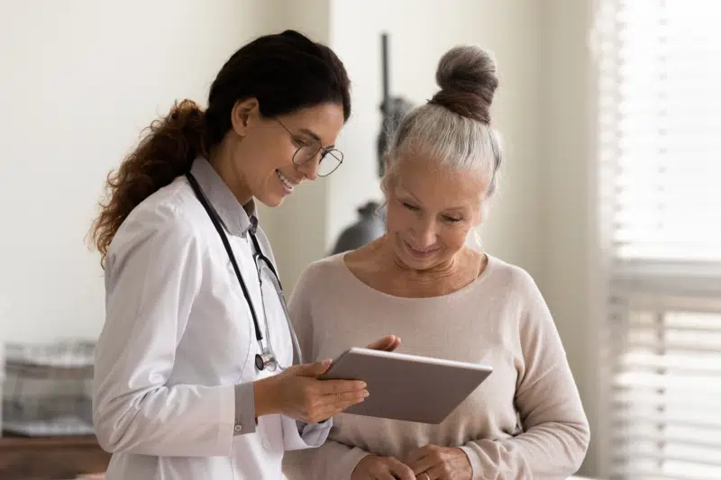 Happy doctor and senior patient use tablet at consultation