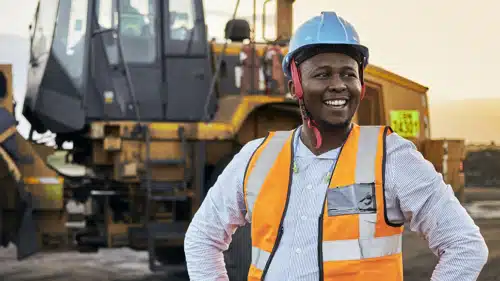 A young Black African coal mine foreman looking off camera laughing wearing reflective bib and hard hat