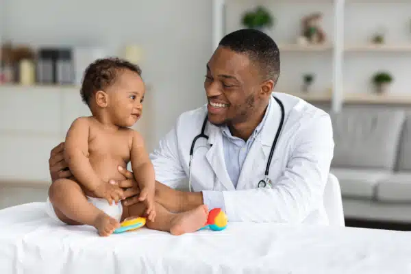 Smiling black doctor checking a little infant baby boy.
