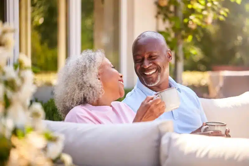 Retired Couple Sitting Outdoors At Home Having Morning Coffee Together