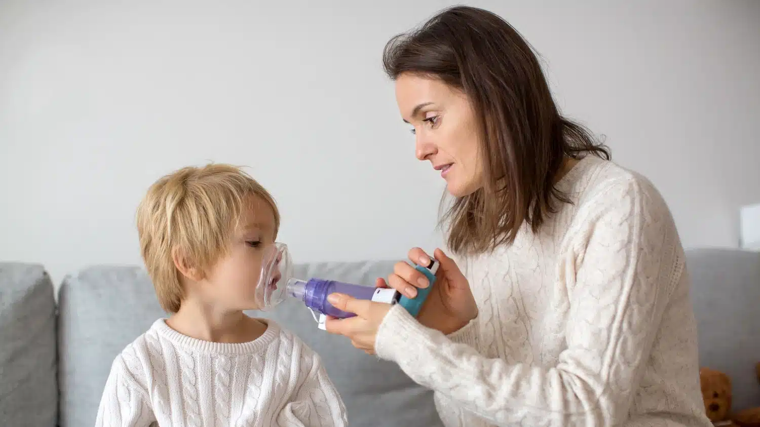Young mother giving asthma inhaler to her child