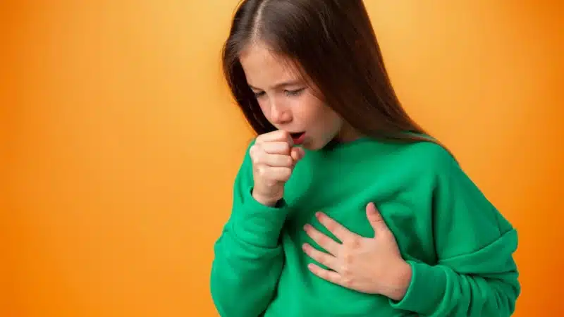 Teen girl wearing casual clothes feeling unwell and coughing against orange background