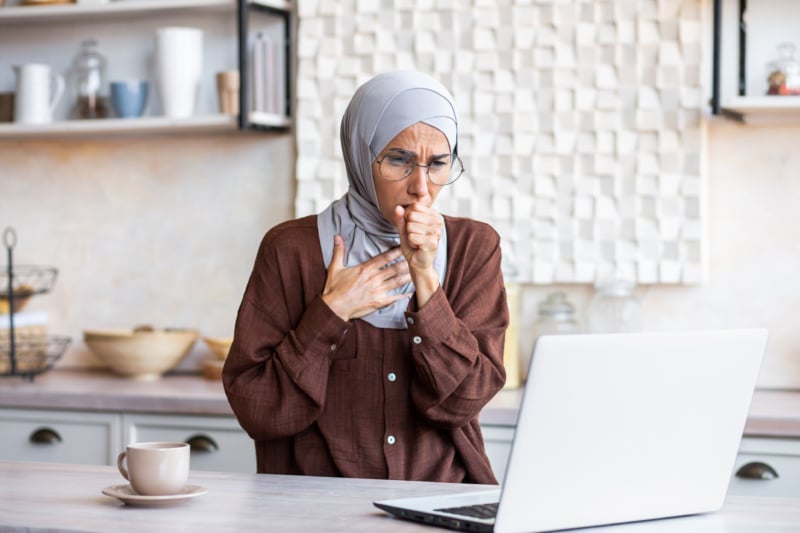 woman coughing and holding her throat while working.