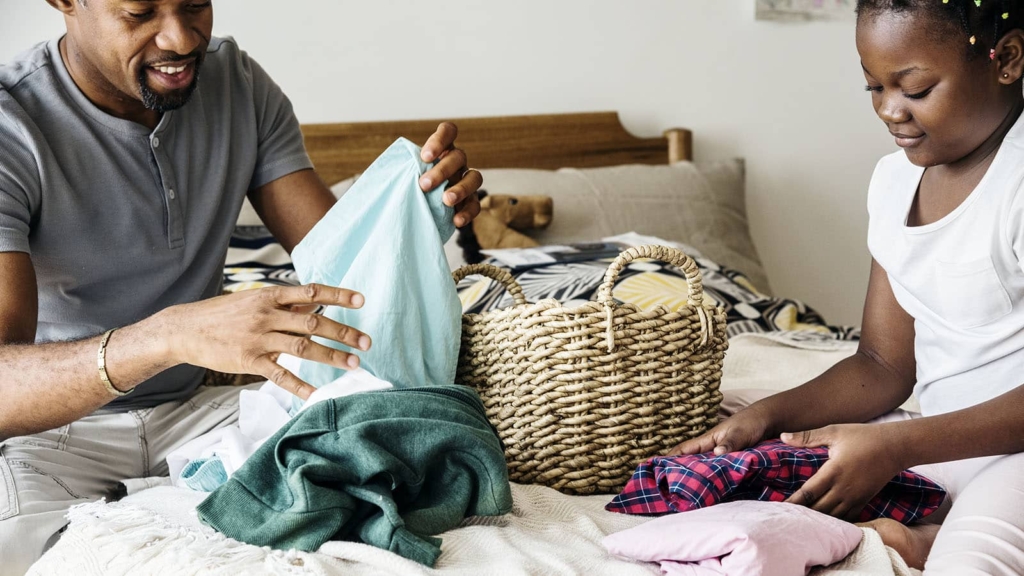 Father and daughter folding laundry on a bed