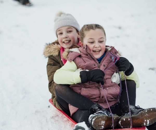 Two little girls are going down a snowy hill together on a sleigh