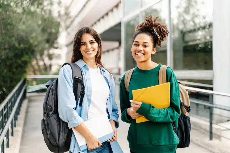 Two female college students smiling ready for classes at the University campus