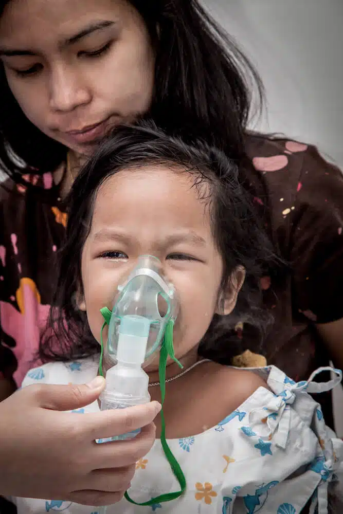 Little girl with severe asthma crying while getting in inhaler mask in hospital