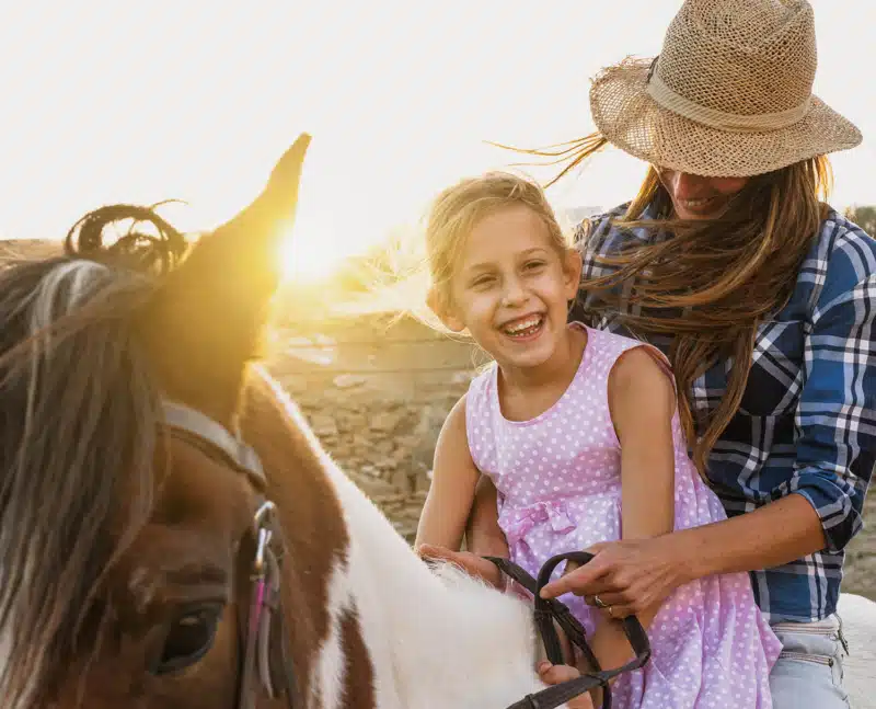 Happy family mother and daughter having fun riding horse inside ranch