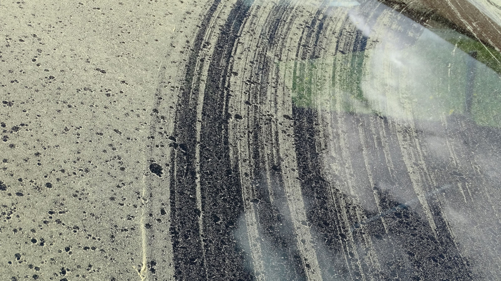 Car windshield covered in yellow pollen with marks of wipers trying to remove the pollen