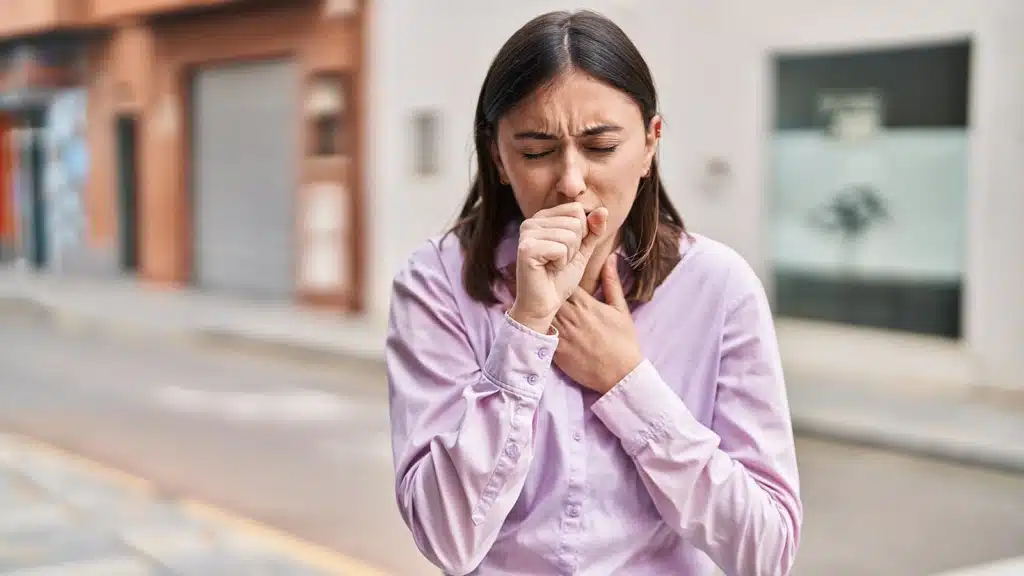 Young woman in the street, coughing covering her mouth with one hand and her chest with the other