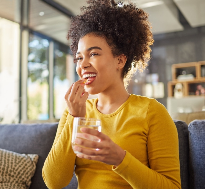 Young happy mixed race woman taking medication with water at home.