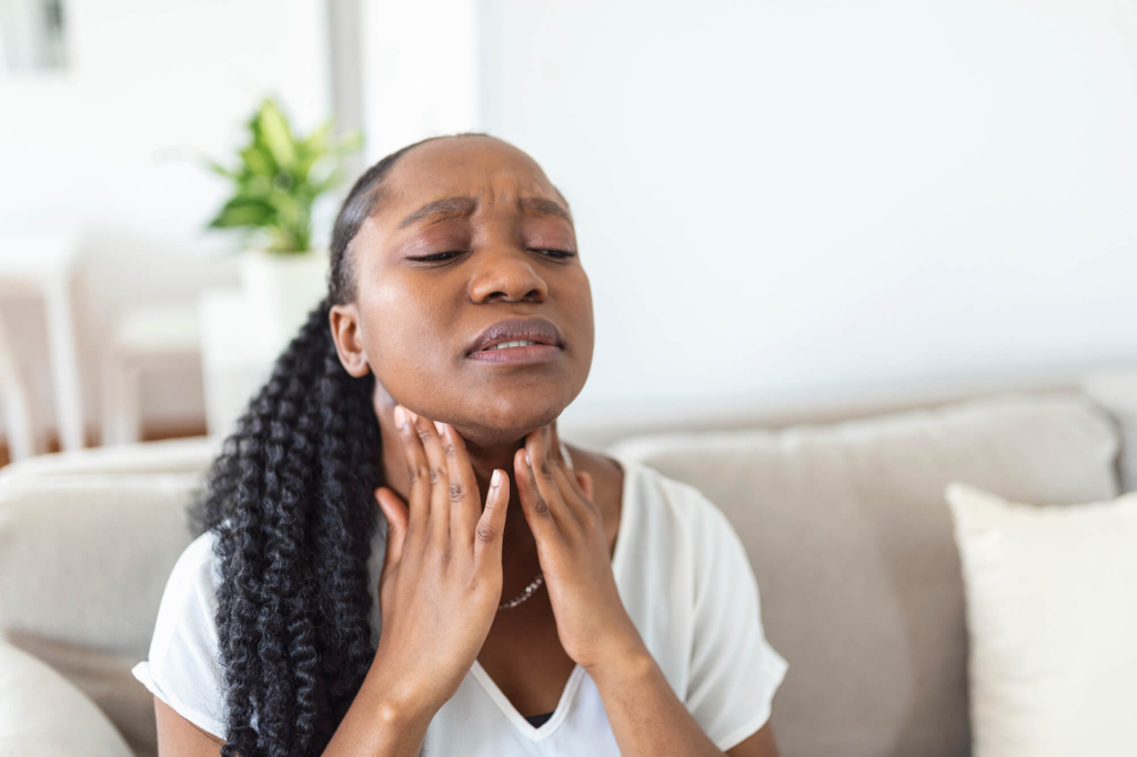 Woman sitting on a couch touching her throat in pain due to airborne food allergies